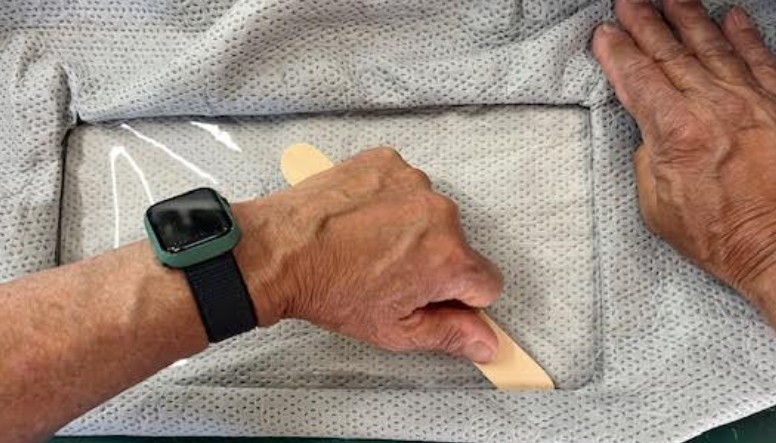 Using wooden craft strip to press fabric tabs into Viraport frame channel